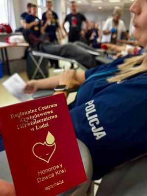Książeczka honorowego dawcy krwi, w tle policjant w mundurze oddaje krew